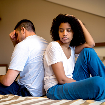 A man and a woman seated on a bed, visibly upset